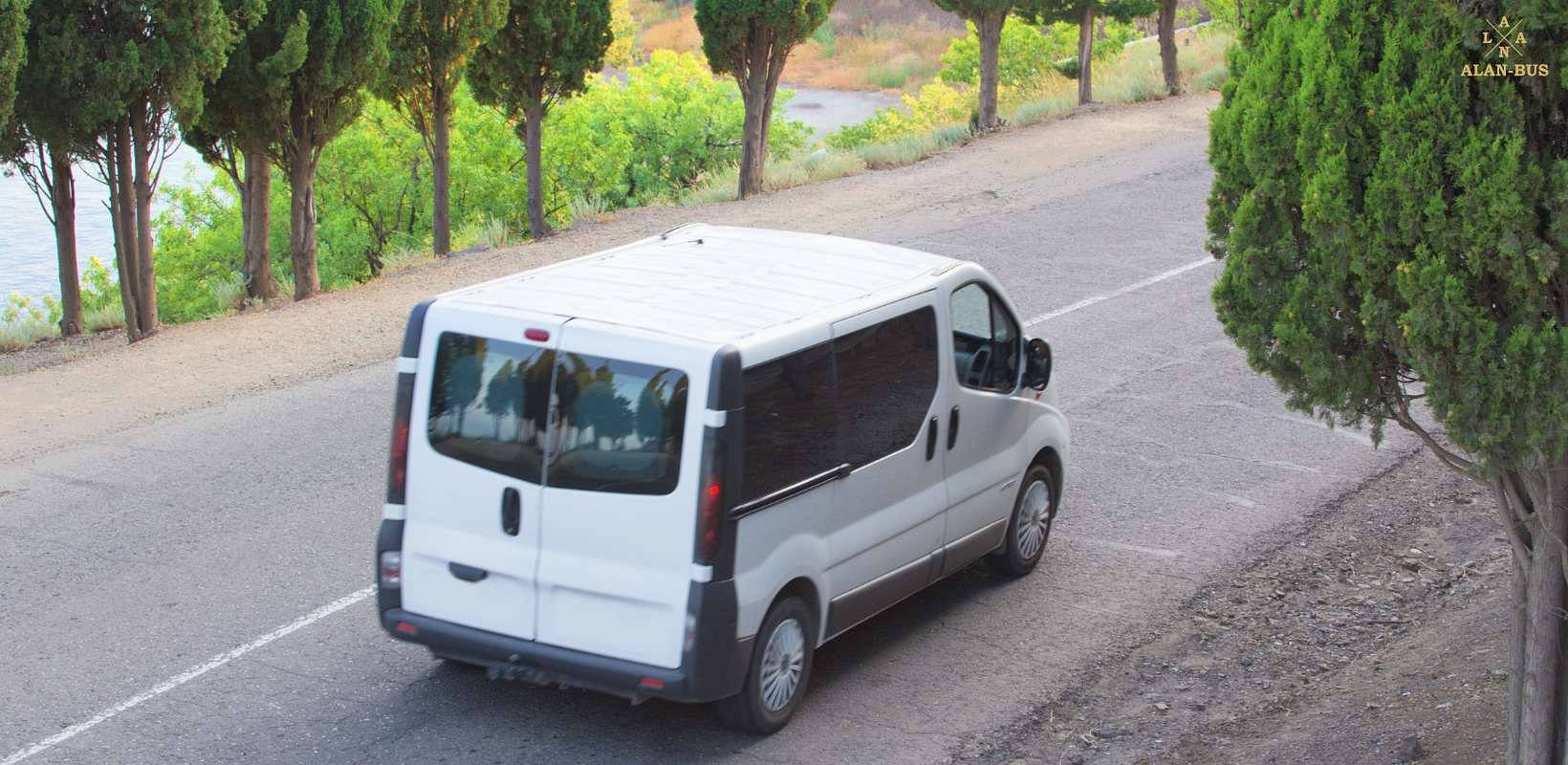Bus ALAN Bus porusza się boczną drogą wśród drzew, w kierunku malowniczego krajobrazu nad wodą.jpg