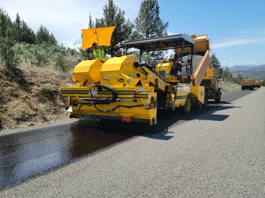a yellow truck driving down a road next to a forest